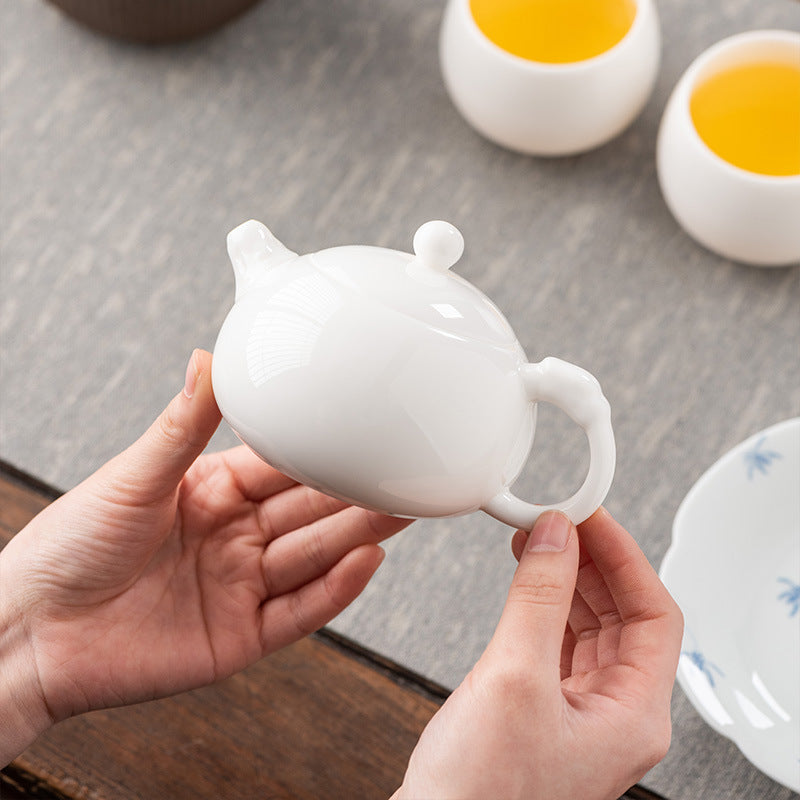 Close-up of a 160ml Dehua Mutton Fat Jade Xishi teapot held between two hands, highlighting its moist, jade-like porcelain texture and ergonomic scale.