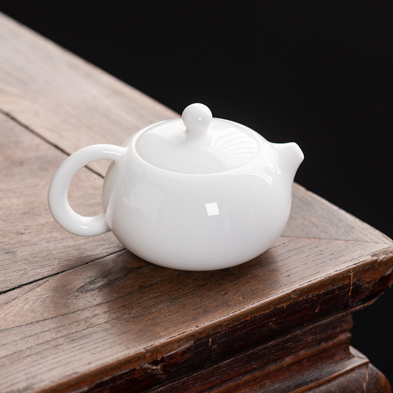 Aesthetic lifestyle view of a Dehua Mutton Fat Jade white porcelain Xishi teapot resting on a natural wooden tea table corner