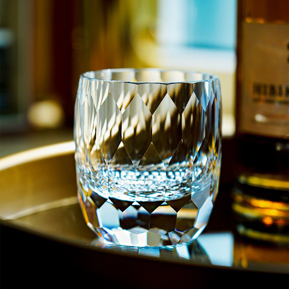An empty Edo Kiriko inspired diamond-cut crystal glass sitting on a bar surface, displaying optical clarity and geometric facets next to a whisky bottle.