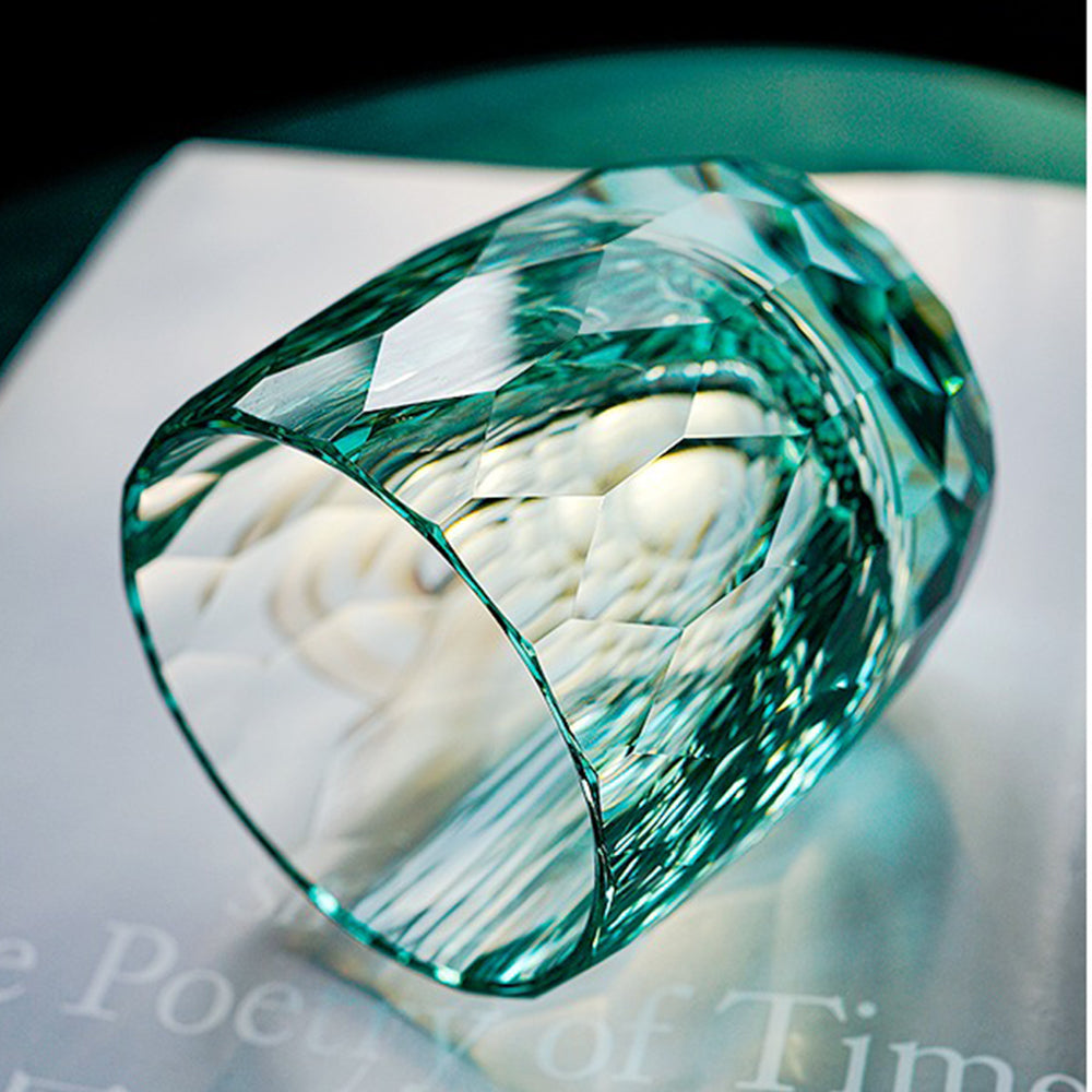 An Edo Kiriko inspired diamond-cut crystal glass resting horizontally, showcasing light green hues, a thick heavy base, and 64 light-refracting facets.
