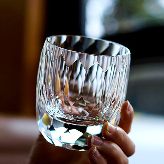 A hand holding an empty Edo Kiriko inspired crystal whisky glass, highlighting the heavy base and 64 diamond-cut light facets.